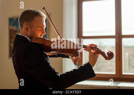 un giovane professionista di talento suona con grazia il violino, un bel musicista in una tuta elegante e formale esegue musica classica Foto Stock