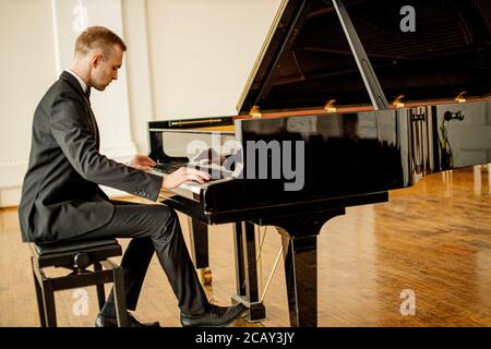 il giovane e bel caucasico in elegante abito formale suona con grazia il pianoforte, mentre il pianista professionista esegue musica classica Foto Stock