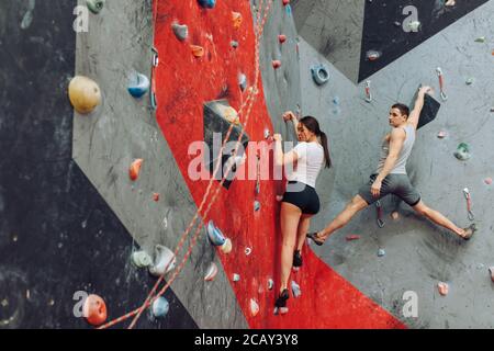 Giovane donna che impara rockclimbing. Uomo muscolare che dà istruzioni e sostegno donna in forma. Foto Stock