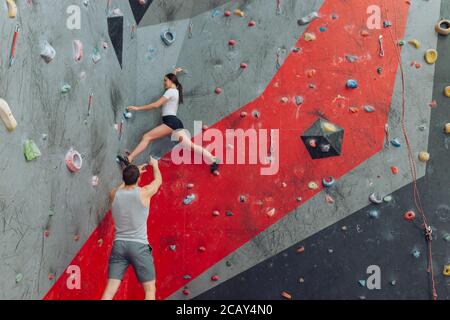 Attraente arrampicatore donna determinato a superare l'altezza. Istruttore giovane uomo che indica come spostare.copiare spazio. Camminare sulla parete Foto Stock