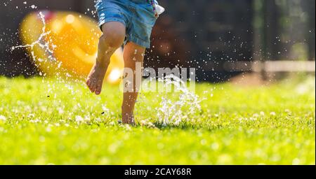 Bambino felice che corre attraverso l'acqua bagnata sprashinh del prato. Foto Stock