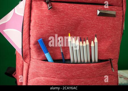 Matite colorate, un pennello e una penna blu si affacciano da una tasca della borsa della scuola. Preparazione per la scuola. Foto Stock