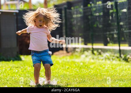 Bambino felice che corre attraverso l'acqua bagnata sprashinh del prato. Foto Stock