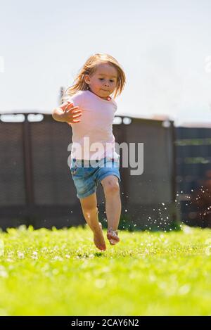 Bambino felice che corre attraverso l'acqua bagnata sprashinh del prato. Foto Stock