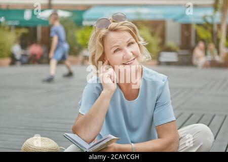 Sorridente donna bianca caucasica anziana di circa 62 anni ha un riposo nel parco pubblico. Lei sembra allegra, felice e amichevole donna anziana vestito in casual Foto Stock