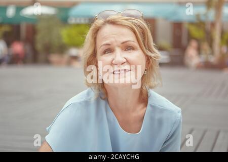 Ritratto di anziana donna caucasica bella circa 62 anni in parco pubblico. Sorride e sembra una donna attiva, allegra e felice. Indossa occhiali da sole Foto Stock