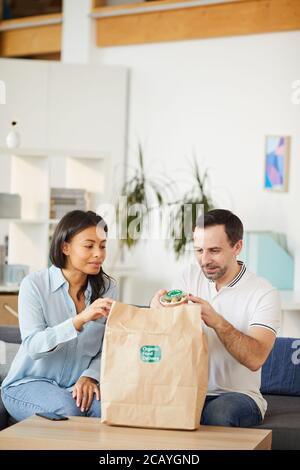 Ritratto verticale di uomo e donna che apre la borsa per la consegna del cibo mentre ti godi il pranzo da asporto in ufficio Foto Stock