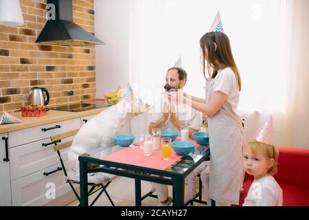 la famiglia caucasica consisteva di madre, padre, figli carini e il loro cane bianco amico famiglia festeggiava il parto insieme a casa, in cucina Foto Stock