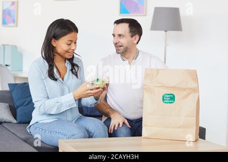 Ritratto di sorridente uomo e donna che apre la borsa per la consegna del cibo mentre ti godi il pranzo da asporto in ufficio o a casa, copia spazio Foto Stock