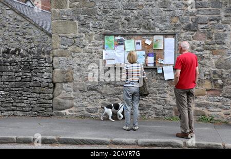 Coppia locale che legge la bacheca di avviso del villaggio a Youlgrave vicino Bakewell nel Peak District Foto Stock