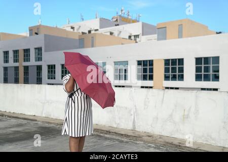 Donna nascosta dietro un ombrello rosso. Concetto creativo urbano. Spazio di copia. Foto Stock