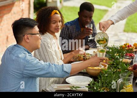 Gruppo multietnico di giovani che sorseggiano bevande mentre si gusta la cena con amici e familiari all'aperto durante la festa estiva, spazio fotocopie Foto Stock