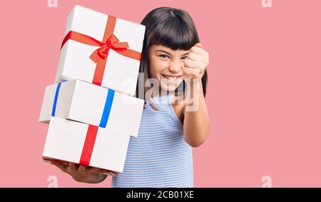 Giovane bambina con bang che tiene i regali infastiditi e frustrati gridando con rabbia, urlando pazzo con rabbia e mano sollevata Foto Stock