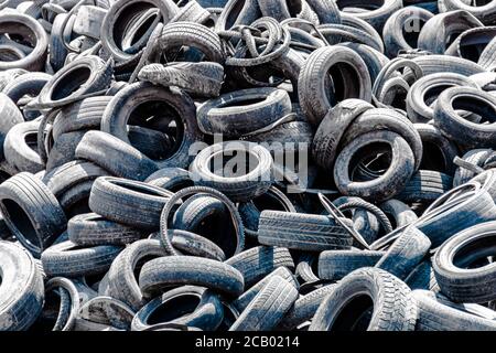 Pile assortite di pneumatici per auto vecchi e usati, che mostrano una varietà di modelli di battistrada in un deposito di pneumatici. Nessuna gente. Spazio di copia Foto Stock