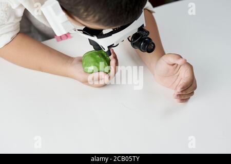 Un ragazzo in testa con lenti d'ingrandimento imparare incredibile chimica degli slime. Gioco tattile o sensoriale per i bambini più grandi Foto Stock