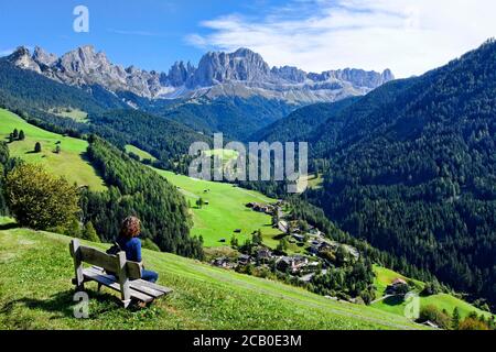 Donna seduta su panchina con vista sul gruppo di Rose Garden Mountain con Villaggio in primo piano, Tires, Tires, Alto Adige, Italia Foto Stock