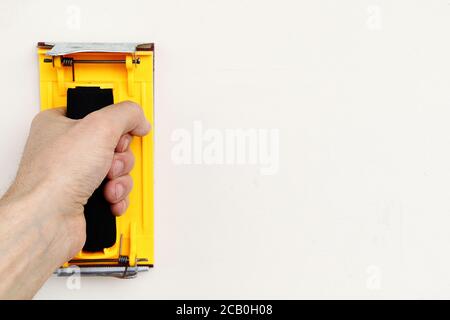 Il supporto di carta vetrata gialla in mano sulla parete bianca con spazio di copia Foto Stock