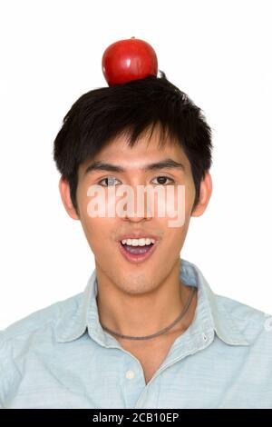 Studio di un giovane bell'uomo asiatico che tiene la mela parte superiore della testa isolata su sfondo bianco Foto Stock