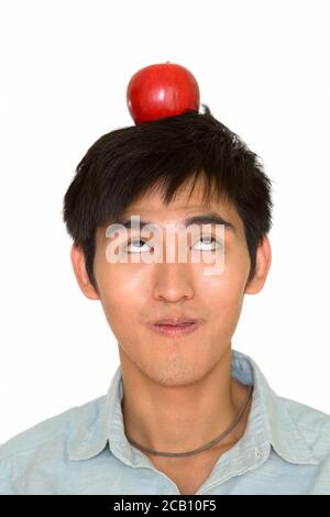 Studio di un giovane bell'uomo asiatico che tiene la mela parte superiore della testa che guarda in alto isolato su sfondo bianco Foto Stock