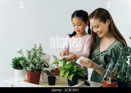 Madre asiatica insegnando bambina come a cura di piante al chiuso. Concetto di attività di legame della famiglia con un bambino. Foto Stock