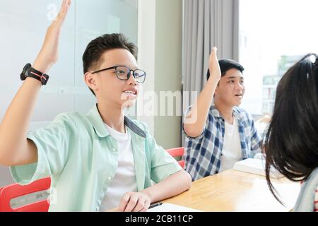 Studenti intelligenti che alzano le mani per mostrare agli insegnanti che sanno la risposta alla sua domanda Foto Stock