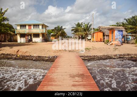 Hopkins / Belize - 10 ottobre 2016: Molo di legno sulla spiaggia di fronte a case colorate nella città costiera Foto Stock