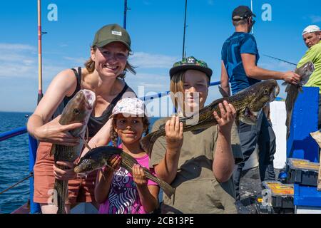 Malmo, Svezia - 6 agosto 2020: Una famiglia in un viaggio di pesca mostra il loro pescato fresco di merluzzo. Oceano blu e cielo sullo sfondo Foto Stock