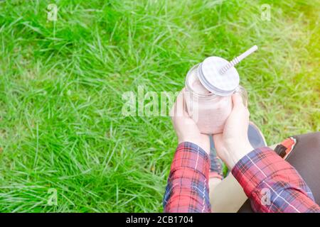 Frullati di fragole in mano femminile su uno sfondo di verde erba Foto Stock