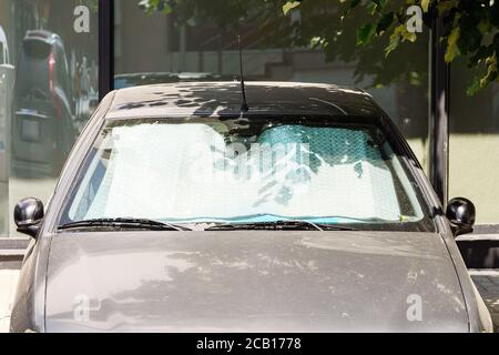 I parasole sotto il parabrezza proteggono l'auto grigia dal sole mentre si parcheggia all'aperto un giorno. Protezione solare in lamina realizzata in materiale riflettente metallico. Foto Stock