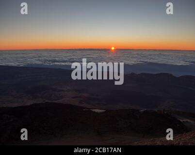 il sole rosso dell'alba che sorge all'orizzonte dalle nuvole bianche la cima del pico del teide vulcano montagna spagnola più alta sull'isola canarie di tenerife Foto Stock