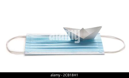 Viaggiare durante la crisi pandemica. Maschera chirurgica con carta bianca spedire su sfondo bianco. Foto Stock