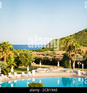 Piscina ad acqua vuota con lettini e ombrelloni. Paesaggio mediterraneo. Lussuosa vista panoramica sul Mar Mediterraneo. Sardegna. Italia. Foto Stock