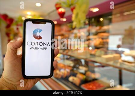 La mano tiene smartphone con Corona WARN-APP nel panificio, Corona Crisis, Stoccarda, Baden-Wuerttemberg, Germania Foto Stock