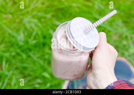 Frullati di fragole in mano femminile su uno sfondo di verde erba Foto Stock