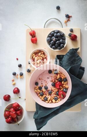 Recipiente per la colazione con yogurt, mirtilli, ciliegie e fiocchi su un tavolo grigio, piatto Foto Stock