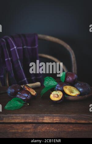 Prugne viola su un tavolo scuro e sedia vintage in lo sfondo Foto Stock