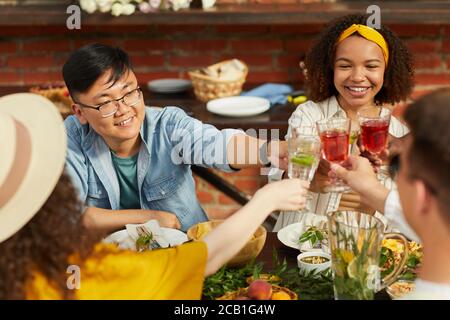 Gruppo multietnico di amici che brindano mentre si gusta la cena all'aperto in estate, concentrarsi sul giovane asiatico sorridendo allegro, spazio copia Foto Stock