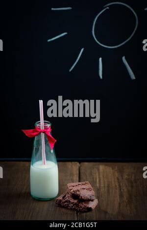 Una bottiglia di latte su un tavolo di legno con brownie al cioccolato torta in primo piano Foto Stock