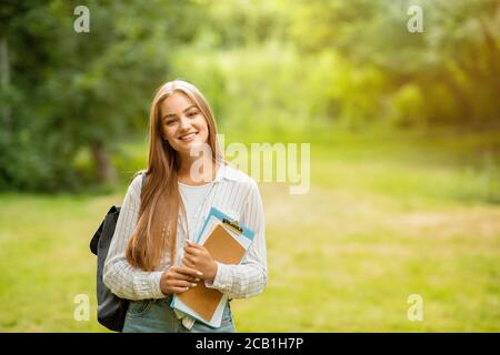 Outdoor Ritratto di Smiling College Student Girl con zaino e. Cartelle di lavoro Foto Stock