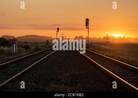 binari ferroviari in campagna durante una bella alba nebbiosa Foto Stock