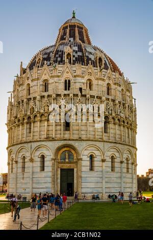 Grande ritratto del famoso Battistero Cattolico Romano di San Giovanni a Pisa al tramonto. La gente sta camminando verso l'ingresso del battistero sul... Foto Stock