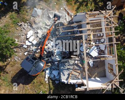 Distruggere la vecchia casa utilizzando benna escavatore nel villaggio. Demolire un. La distruzione della vecchia casa l'escavatore. Vista dall'alto. Colpo di drone. Foto Stock