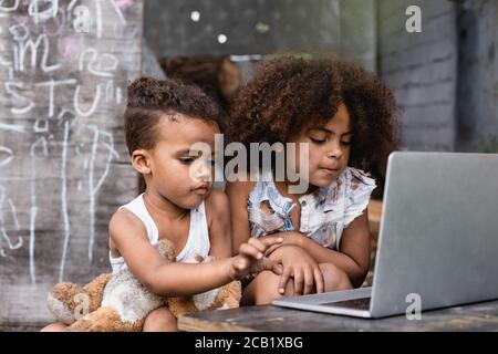 focalizzazione selettiva dei poveri bambini afro-americani che usano il laptop all'esterno Foto Stock