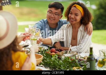 Ritratto di giovane coppia mista che brinda mentre si gusta la cena con gli amici all'aperto al Summer Party, copy space Foto Stock