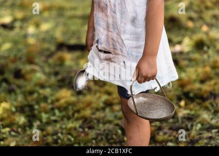 Vista ritagliata del povero bambino afroamericano che tiene la piastra di metallo e cucchiaio su strada urbana Foto Stock