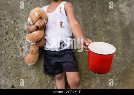 Vista ritagliata del ragazzo afro-americano con orsacchiotto elemosina in baraccopoli Foto Stock