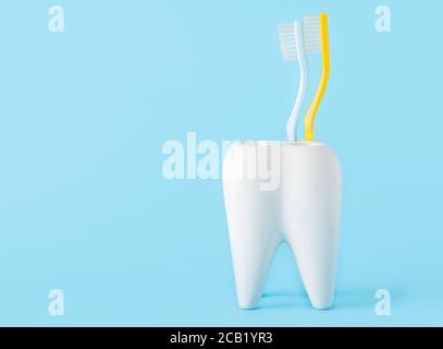 Due spazzolini da denti in un bicchiere a forma di dente sopra uno sfondo blu Foto Stock