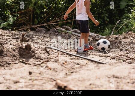 Vista ritagliata di un bambino afro-americano che gioca a calcio strada sporca in baraccopoli Foto Stock