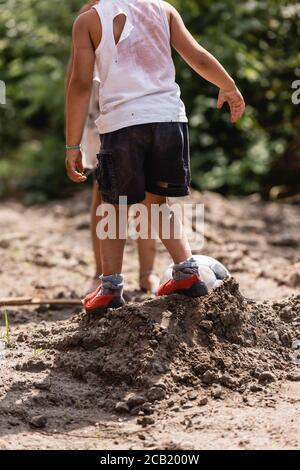 Vista ritagliata di bambini afro-americani disperati che giocano a calcio strada sporca in baraccopoli Foto Stock