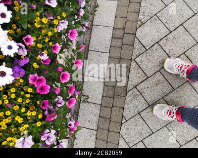 persona in piedi accanto ad un bel vaso giardino fiorito pieno di petunias e di altri fiori graziosi Foto Stock
